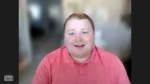 Smiling man in a pink polo on a video call with a blurred background.