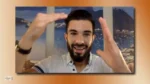 Smiling man on a video call frames a shot with his hands against a coastal backdrop at the window.