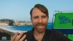 Smiling man with brown hair and beard on a video call, ocean coastline behind him and a green vehicle with a slogan nearby.