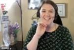 Smiling woman with a headset on a video call in a home-office, certificates on the wall and office decor; 'The Nonprofit Show' watermark.