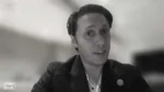 Man in a blazer speaks in a grayscale video frame, with a nonprofit show logo bottom-left; appears to be an interview or webinar.