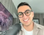 Smiling man with round glasses speaks into a microphone in a home studio setting