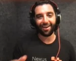 Smiling man with a headset and microphone facing the camera; Nexus logo on his black shirt.