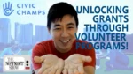 Smiling man in a red shirt extends his hands toward the camera with the headline 'Unlocking grants through volunteer programs' and logos for Civic Champs and The Nonprofit Show in the background, cityscape visible behind them.