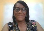Smiling woman with glasses and floral top, posing for a webcam portrait.
