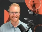 Smiling man with blond hair and glasses speaks into a microphone in a podcast studio.