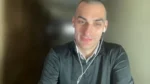 Smiling man with white earbuds on a video call, looking at the camera