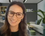 Smiling woman wearing glasses on a video call; modern office backdrop with an ERC sign and plants.