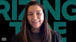 Smiling woman with long dark hair on a video call, background shows bold teal letters.