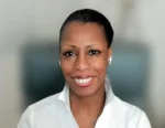 Smiling woman with short hair in a white collared shirt, wearing wireless earbuds, facing the camera.