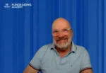 Smiling man in a light blue polo sits against a blue backdrop with the Fundraising Academy logo in the top-left corner.
