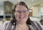 Smiling woman with purple glasses in a cozy living room setting.