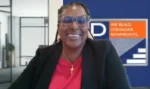 Smiling woman in a video conference wearing a red blouse and black blazer; background shows a nonprofit banner reading 'We Build Stronger Nonprofits'.