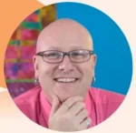 Close-up portrait of a smiling, bald person wearing glasses and a pink shirt, resting their chin on their hand in a circular crop.