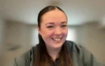 Smiling woman with long brown hair in a video call, blurred background behind her.