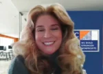Smiling woman with long blond hair in an office, with a nonprofit banner in the background reading 'We Build Stronger Nonprofits'.