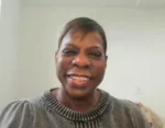 Smiling woman with short hair wearing a gray knit sweater, looking at the camera indoors.