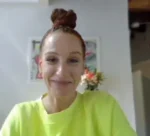Smiling woman with brown hair in a top bun wearing a neon green shirt indoors.