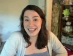 Woman with dark hair smiling at the camera in a cozy room indoors.