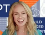 Smiling blonde woman speaking on camera with a blue/orange patterned backdrop behind her (likely a video interview or presentation).