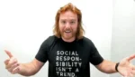 Man with red hair wearing a black T-shirt that reads 'Social responsibility isn't a trend,' gesturing with open arms.